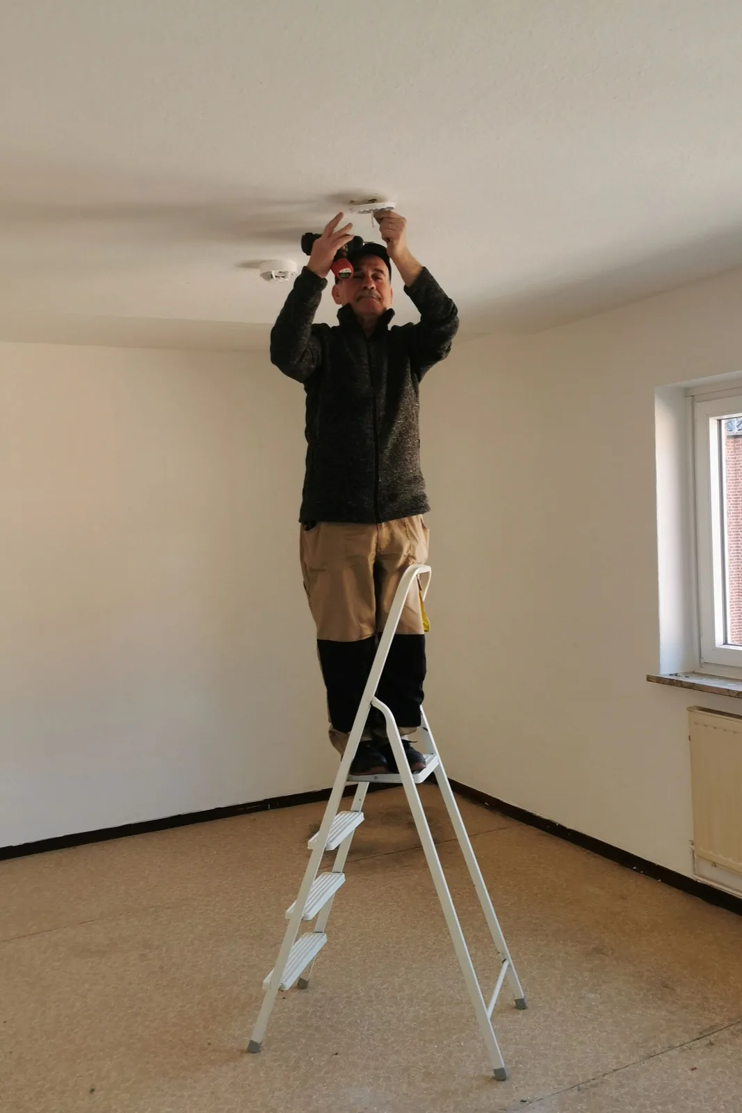 Fitting a ceiling detector from a step ladder, for electrical permit in Abbotsford